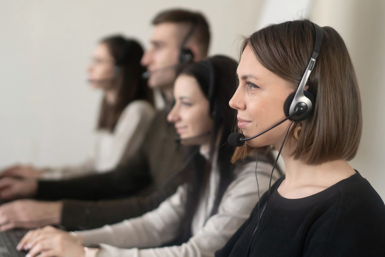 A row of coworkers in headsets work side by side at laptops.