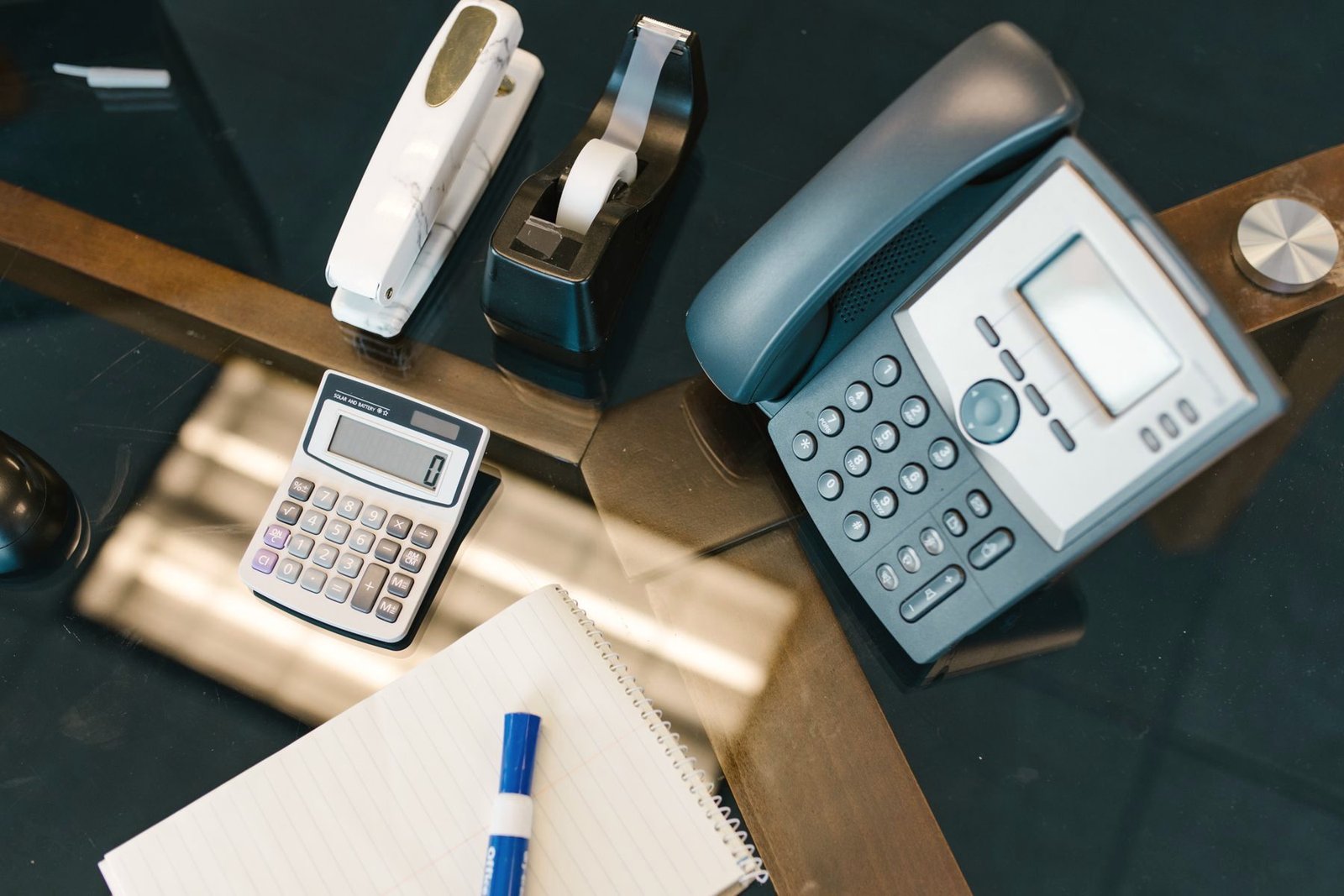 An office desk phone beside a calculator, notepad and pen.