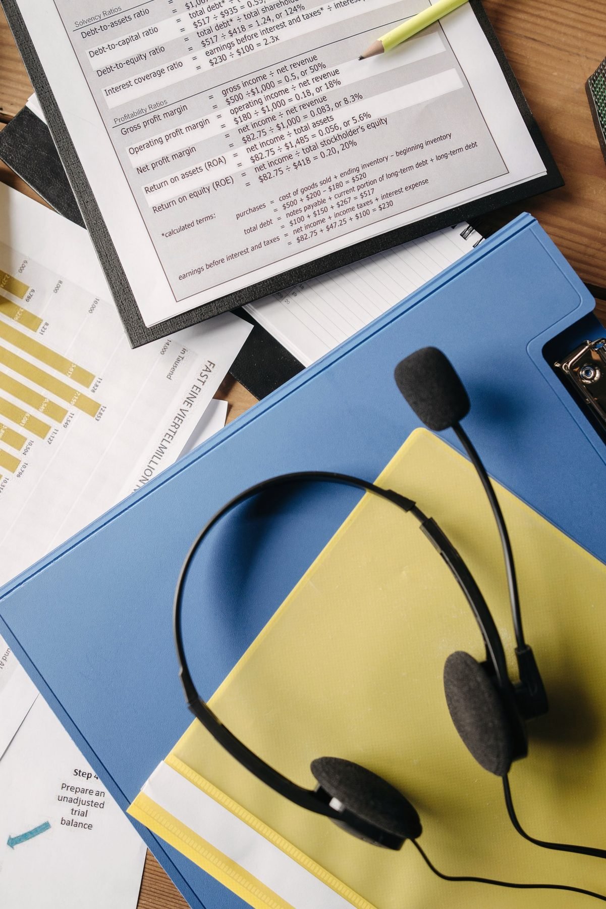 A headset rests on a desk among documents and folders.