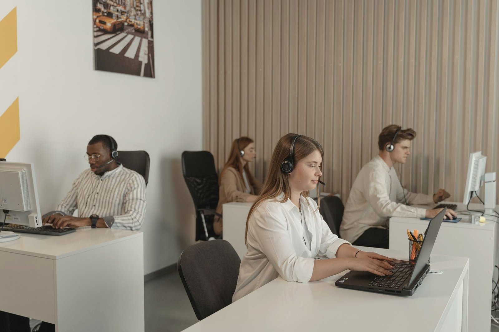 Several operators at a shared office desk taking calls on laptops and headsets.